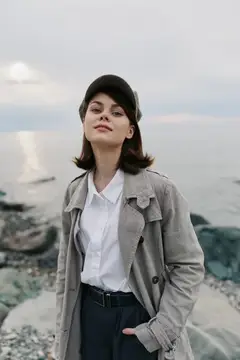 Молодая женщина в плаще и кепке на каменистом берегу моря