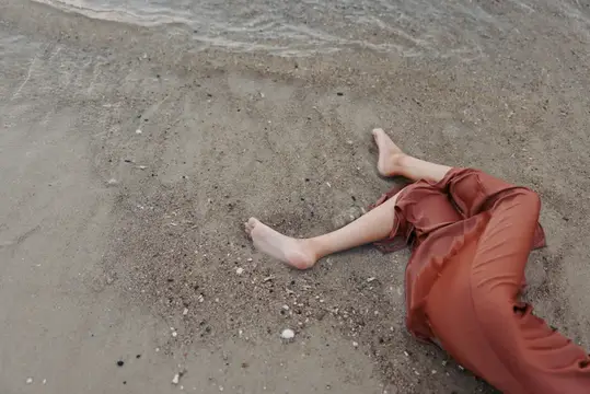 Босые ноги лежащего человека на песке у кромки воды