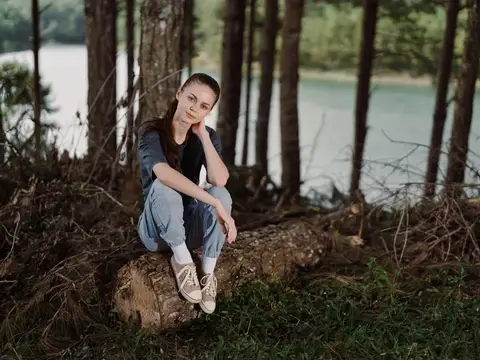 Молодая женщина сидит на бревне в лесу у озера