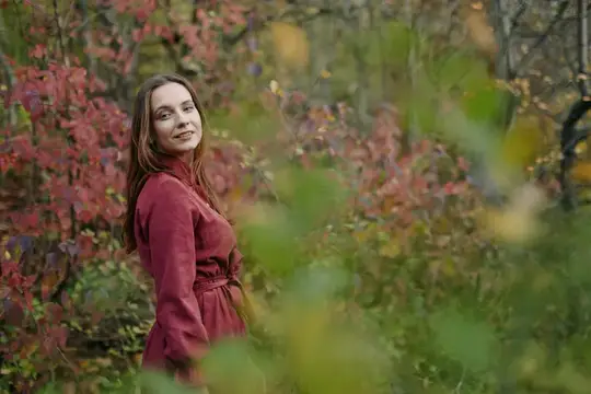 Молодая женщина в бордовом платье улыбается в осеннем лесу