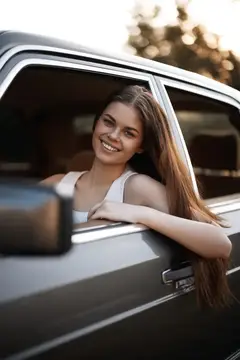 Улыбающаяся девушка с длинными волосами выглядывает из окна автомобиля