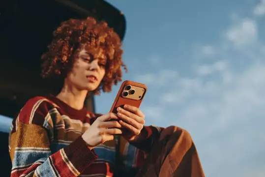 Рыжеволосая девушка с кудрями листает телефон на улице