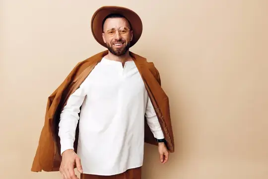 Улыбающийся бородатый мужчина в шляпе и очках на бежевом фоне