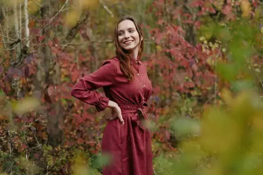 Улыбающаяся женщина в бордовом платье осенью в лесу