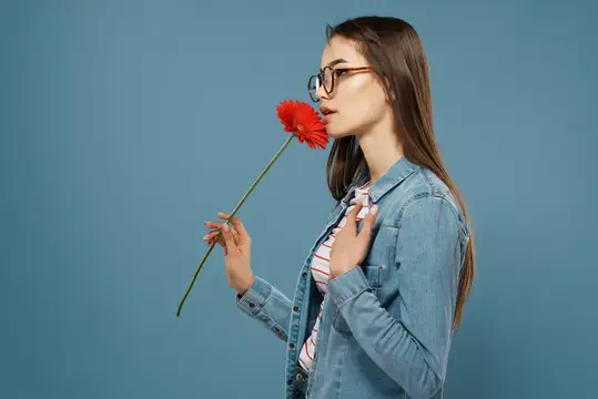 Девушка в очках нюхает красный цветок на синем фоне