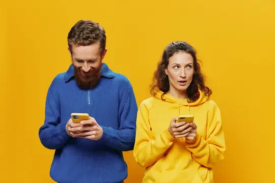 Удивлённая женщина и бородатый мужчина со смартфонами на жёлтом фоне