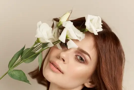Молодая женщина с белыми розами у лица на бежевом фоне