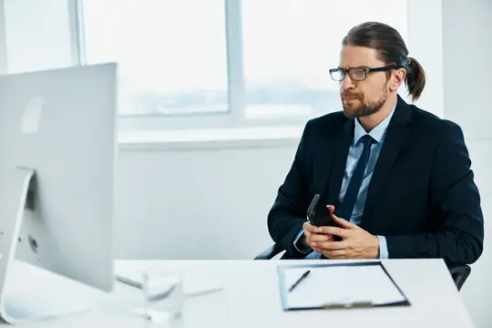 Мужчина в очках с длинными волосами работает в офисе за компьютером