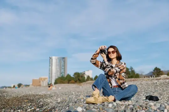 Фотограф отдыхает на солнечном побережье, сидя на гальке с камерой наготове