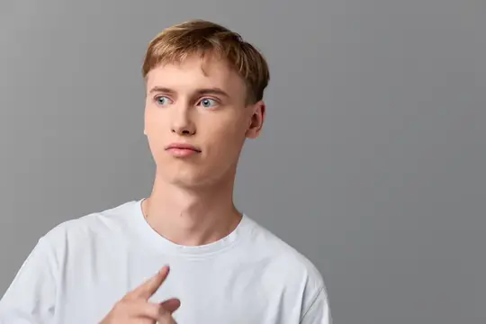 Задумчивый светловолосый парень в белой футболке на сером фоне