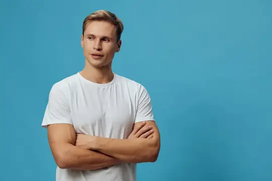Светловолосый мужчина в белой футболке со скрещёнными руками на голубом фоне
