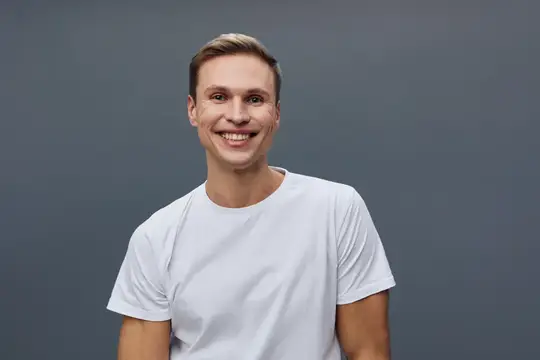 Улыбающийся светловолосый парень в белой футболке на сером фоне