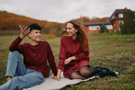 Молодая пара сидит на пледе и весело общается на осенней поляне