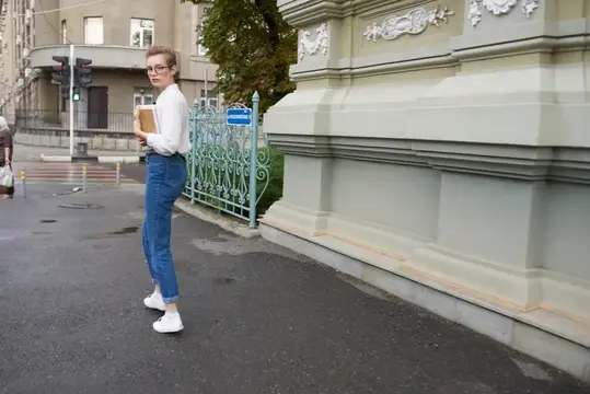 Молодая женщина с книгой стоит на городской улице у старинного здания