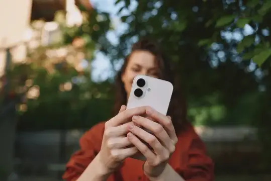 Девушка в красной рубашке держит белый смартфон на улице
