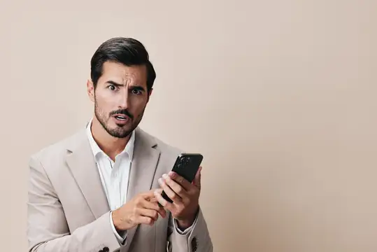 Удивлённый мужчина в бежевом пиджаке смотрит на телефон