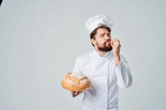 Бородатый пекарь в колпаке пробует свежий хлеб на вкус