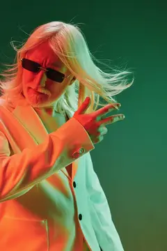 Седой мужчина в солнцезащитных очках и светлом пиджаке на зелёном фоне