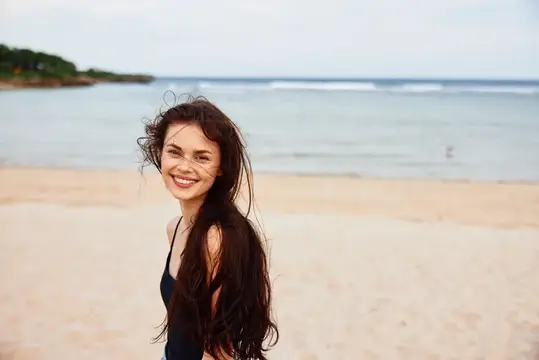 Улыбающаяся темноволосая девушка на песчаном пляже у моря