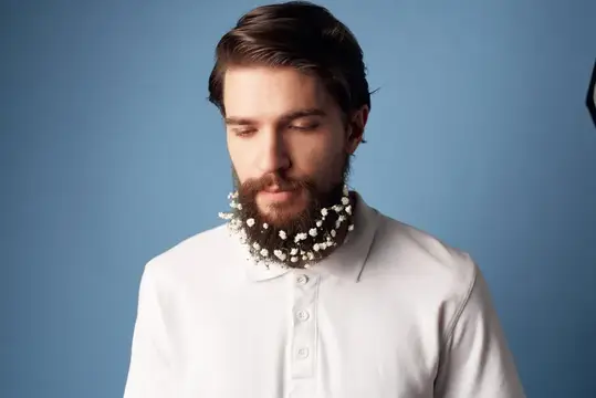 Бородатый мужчина в белой рубашке с белыми цветами в бороде на синем фоне