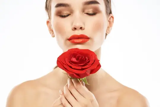 Молодая женщина с красной розой у лица на белом фоне