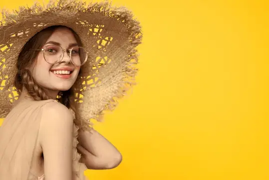 Улыбчивая девушка в соломенной шляпе и очках на жёлтом фоне