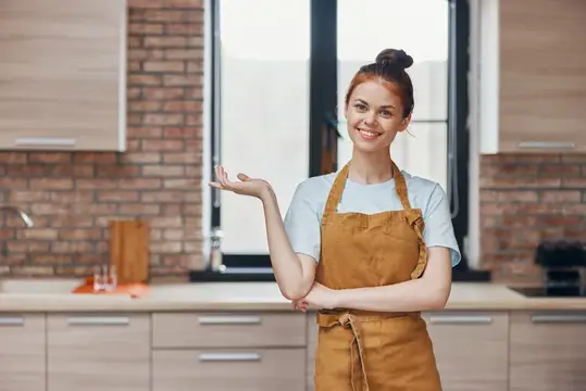 Рыжеволосая девушка в фартуке улыбается на кухне