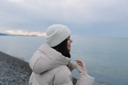 Улыбающаяся девушка в белой шапке смотрит на море