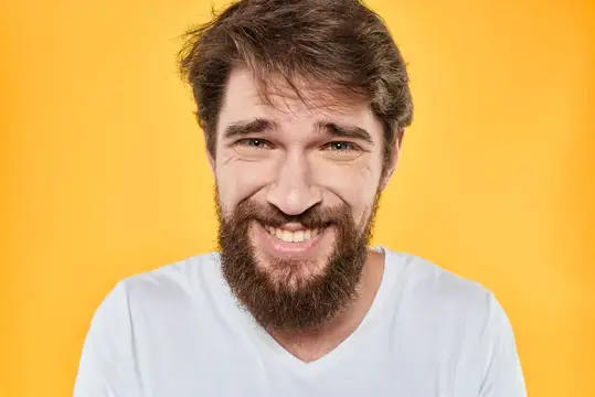 Улыбающийся бородатый мужчина в белой футболке на жёлтом фоне