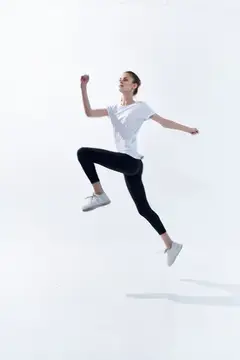 Молодая женщина в спортивной одежде прыгает на белом фоне