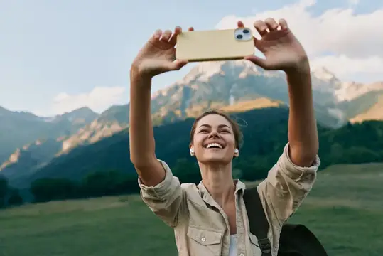 Улыбающаяся девушка фотографирует горы на смартфон