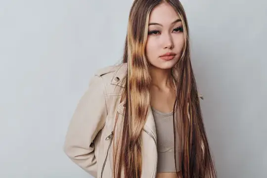 Азиатская девушка с длинными светлыми прядями в бежевой куртке