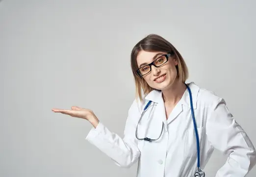 Улыбающаяся женщина-врач в очках и белом халате показывает рукой в сторону