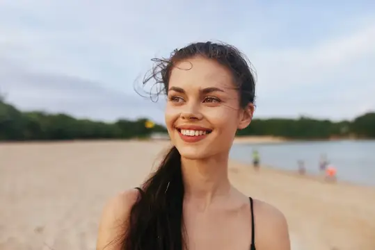 Улыбающаяся темноволосая девушка на песчаном пляже у воды