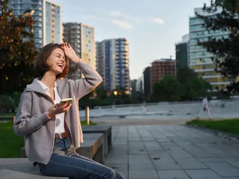 Смеющаяся девушка со смартфоном на городской площади