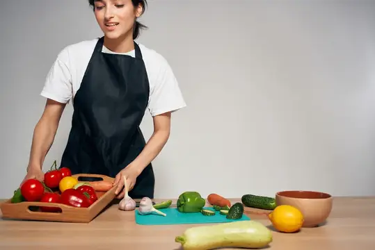 Молодая азиатская женщина в фартуке раскладывает свежие овощи на кухонном столе