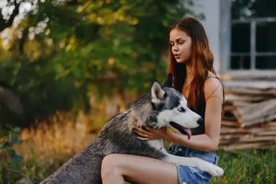 Молодая девушка обнимает хаски на фоне летнего сада