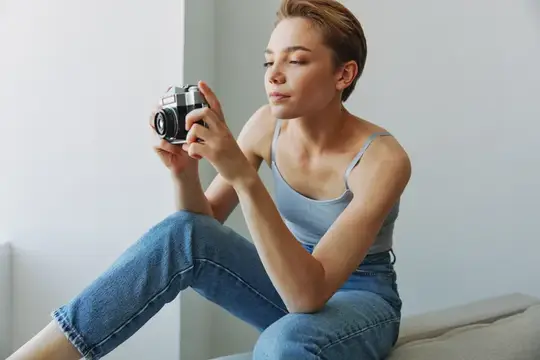 Женщина-фотограф снимает в студии на старую плёночную камеру, сидя дома на диване