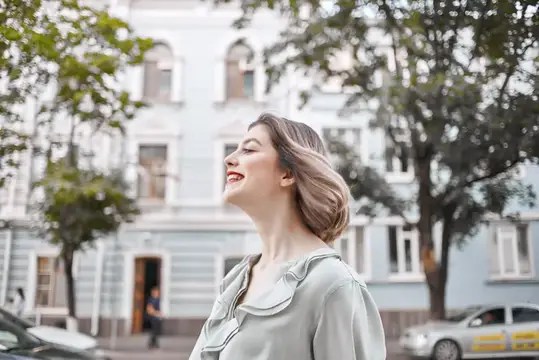 Улыбающаяся женщина с закрытыми глазами на городской улице