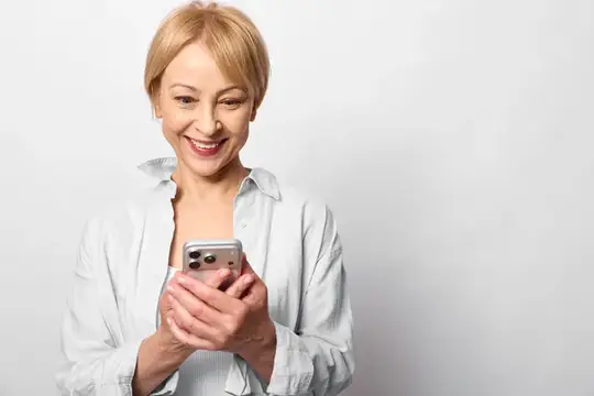 Пожилая женщина улыбается в портрете в помещении, держит смартфон, расслабленная поза