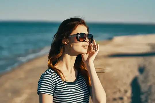 Молодая женщина в солнечных очках улыбается на берегу моря