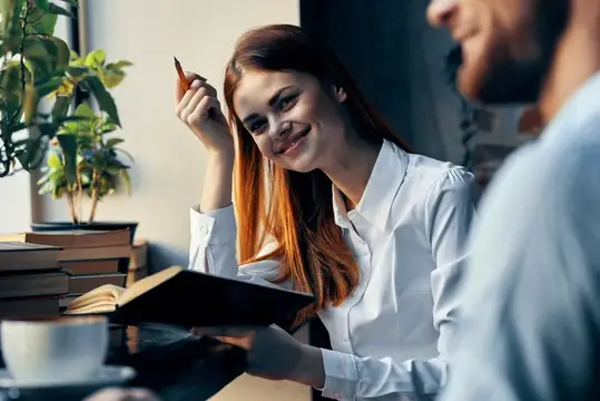 Рыжеволосая девушка с книгой улыбается собеседнику в кафе