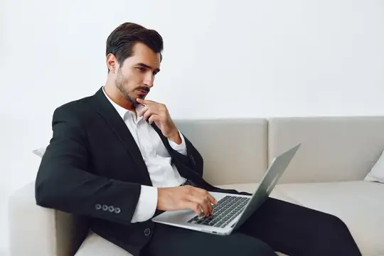 Задумчивый мужчина в костюме работает за ноутбуком на диване