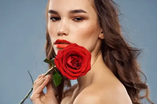 Молодая женщина с красной розой у лица на сером фоне