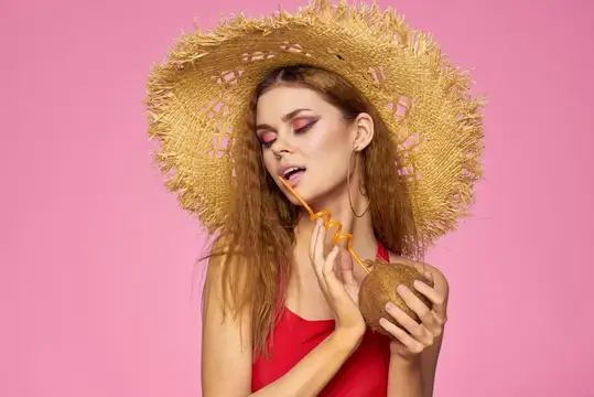 Женщина с кокосовым коктейлем в соломенной шляпе на розовом фоне