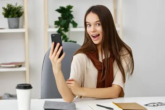 Удивлённая девушка с телефоном в руках за рабочим столом