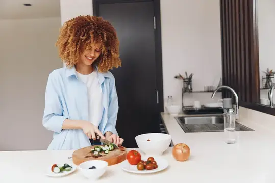 Улыбающаяся темнокожая девушка режет овощи на современной кухне