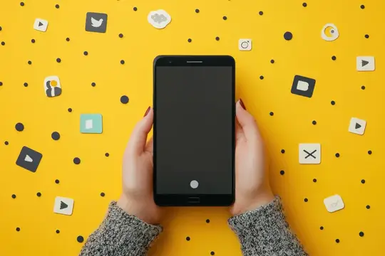 Женские руки держат смартфон с пустым экраном на жёлтом фоне с иконками соцсетей
