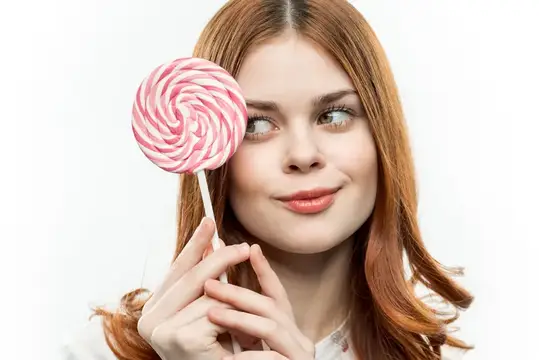 Рыжеволосая девушка с розовой леденцовой карамелью у лица