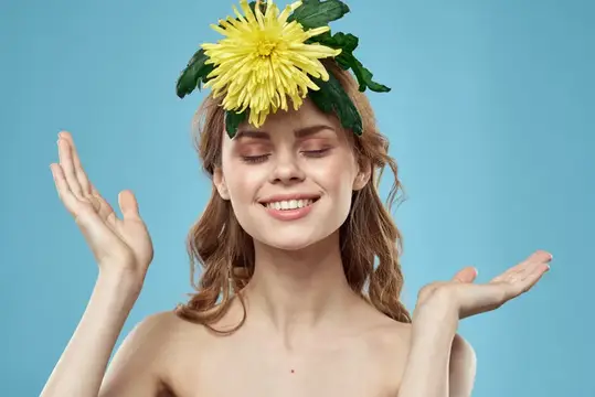 Улыбающаяся девушка с жёлтой хризантемой на голове на голубом фоне